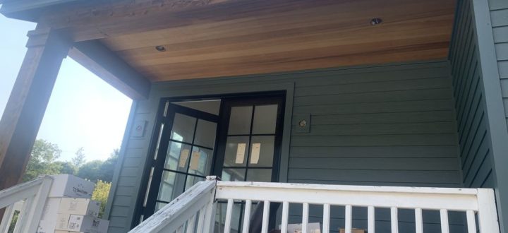 Front entry of a modern home with detailed wooden overhead structure and boxes with building materials, illustrating an upgrade in progress.