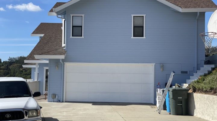 A suburban home with a fresh light blue paint job, featuring a new garage door and clean aesthetic for enhanced curb appeal.