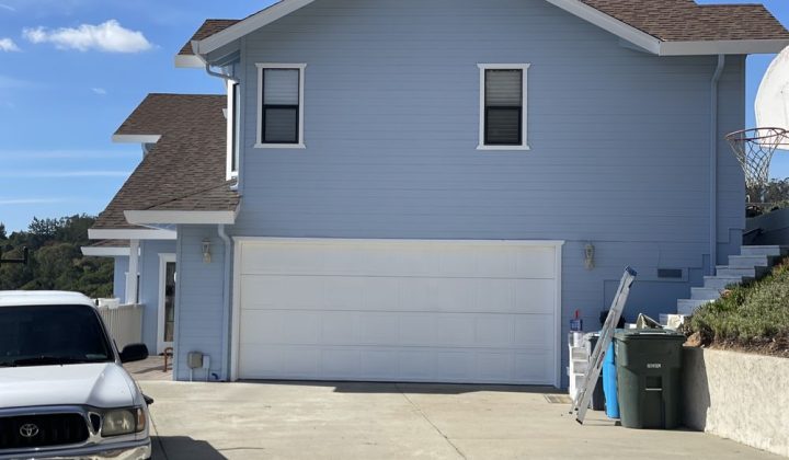 A suburban home with a fresh light blue paint job, featuring a new garage door and clean aesthetic for enhanced curb appeal.