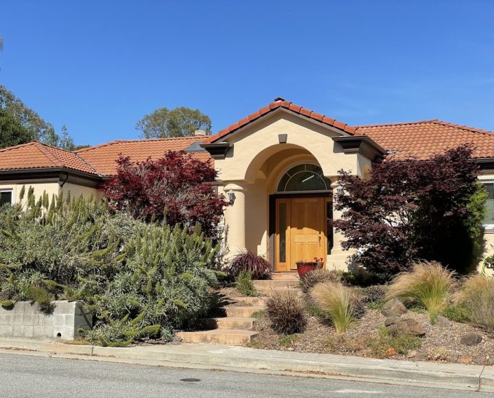 A beautifully landscaped modern house with a Mediterranean-style facade and terracotta roof, showcasing the results of a professional exterior painting job.
