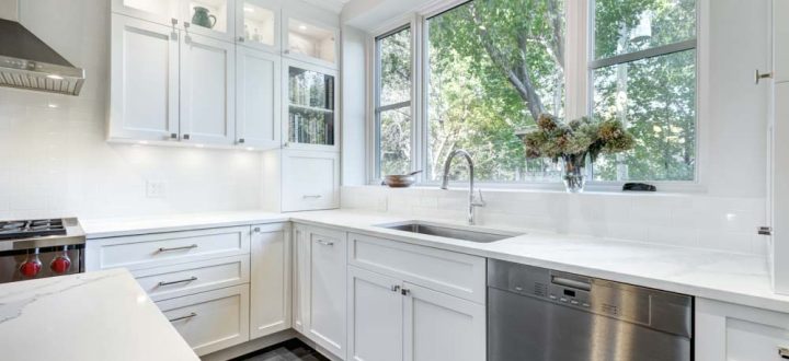 A modern kitchen with white cabinets, stainless steel appliances, and natural light flowing through large windows, providing a clean and inviting cooking space.