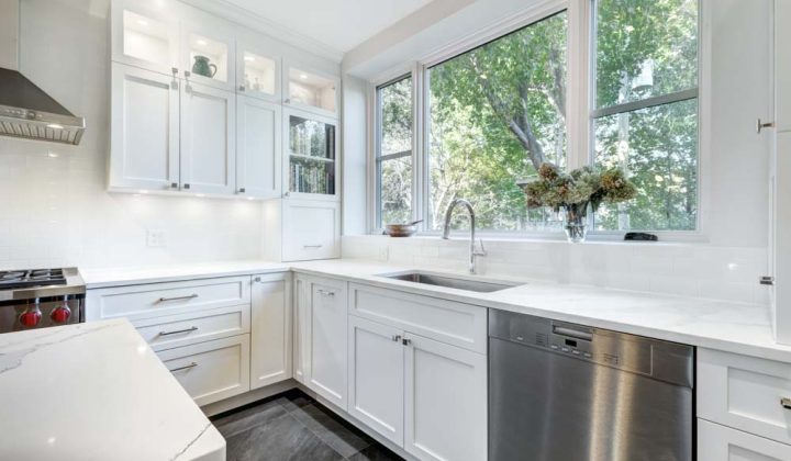 A modern kitchen with white cabinets, stainless steel appliances, and natural light flowing through large windows, providing a clean and inviting cooking space.