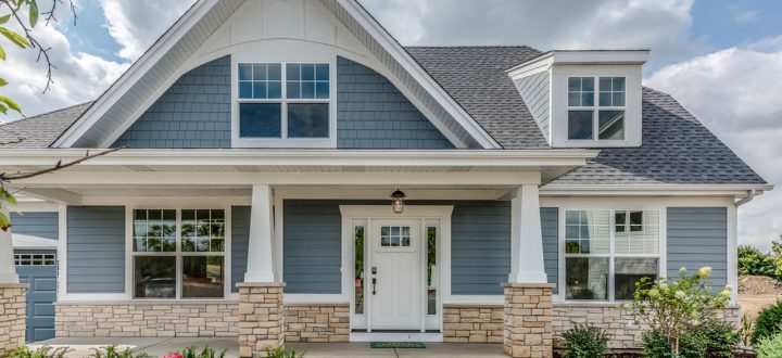 A newly built home with gray siding and white trim, showcasing a welcoming porch with blooming flowers and stone details for a warm, inviting entrance.